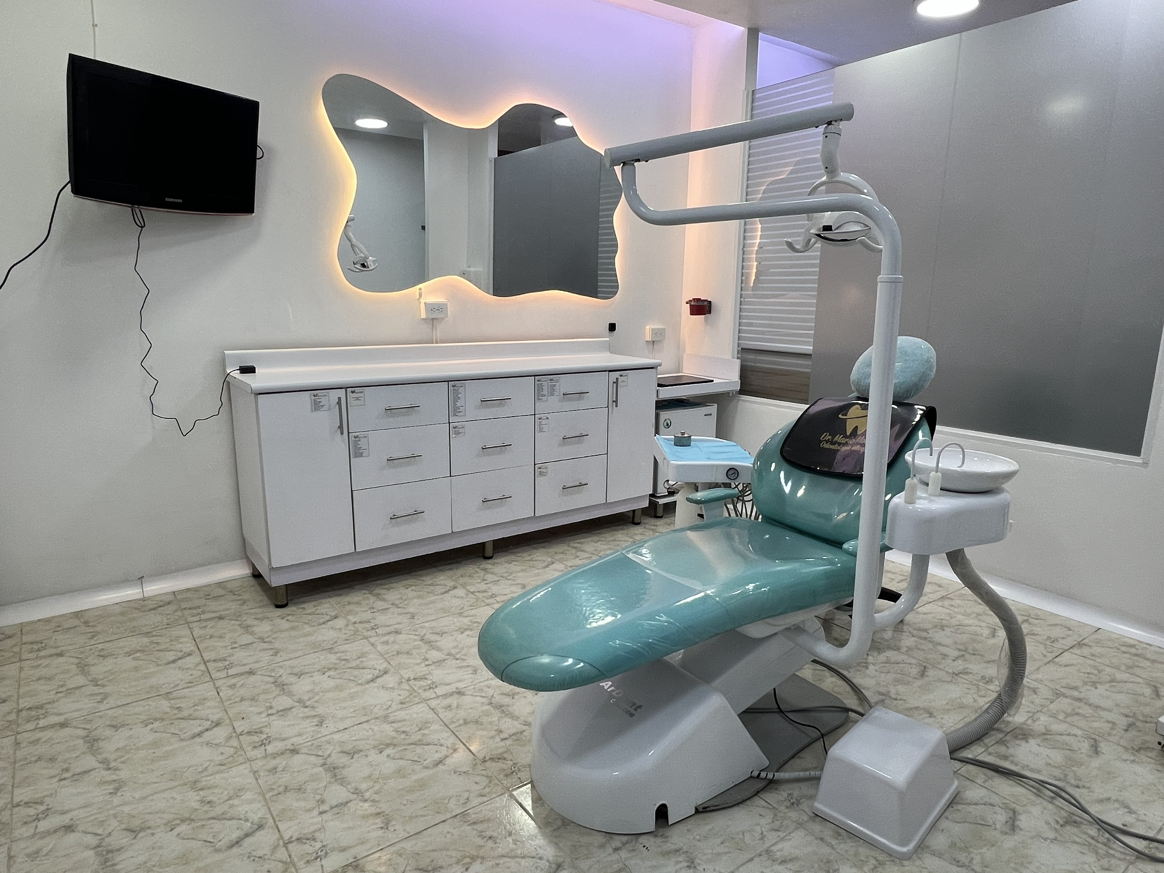 Fotografía real del consultorio dental del Dr. Mario Molina, mostrando el sillón turquesa y el espejo irregular retroiluminado